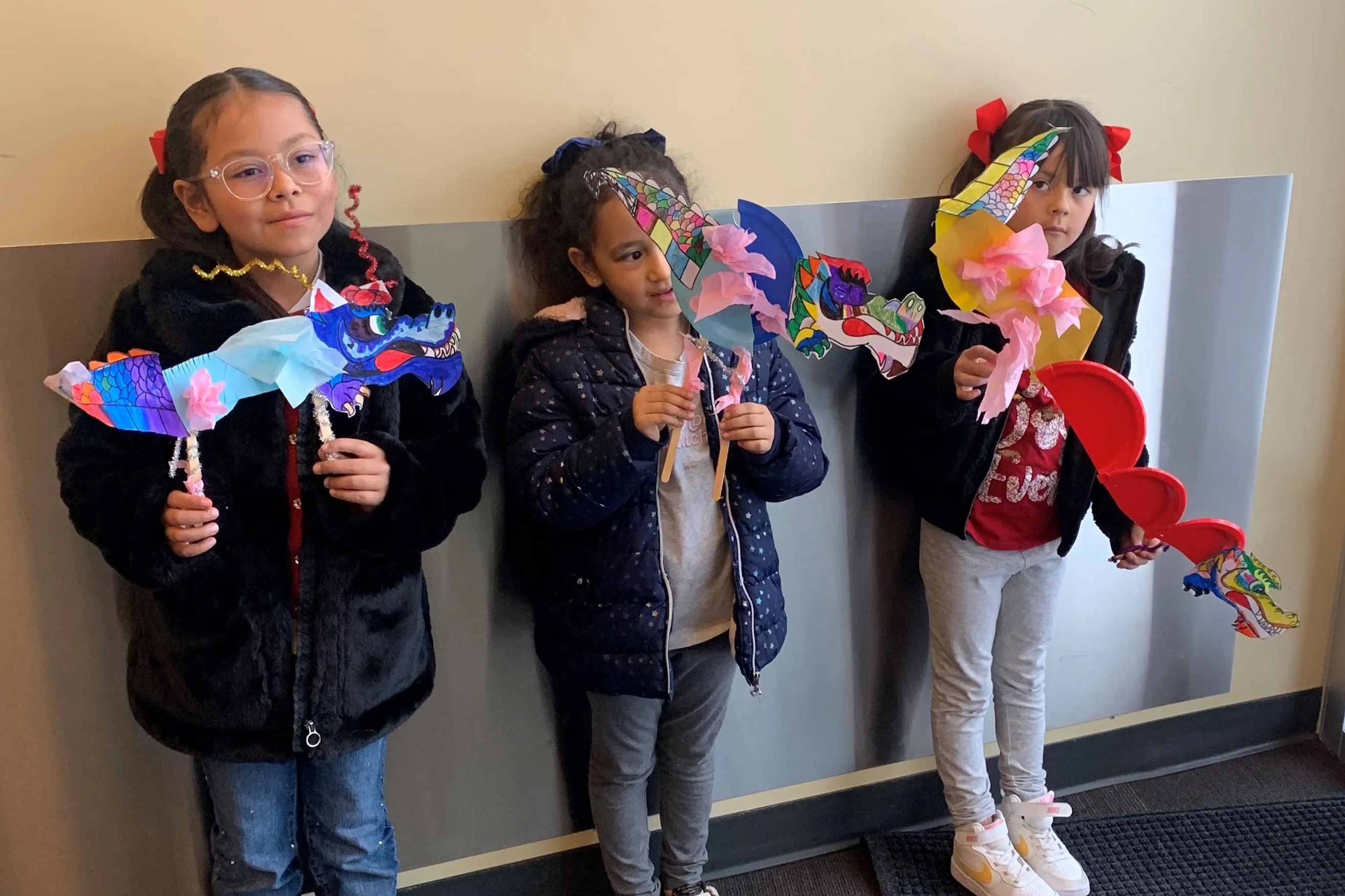 Three children standing, holding colorful paper dragon crafts.